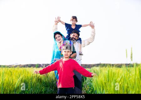 Portrait einer glücklichen, jungen indischen Bauernfamilie, die auf dem Weizenlandwirtschaftsfeld steht, Eltern mit Kindern im Freien, Konzept des ländlichen indiens. Speicherplatz kopieren Stockfoto