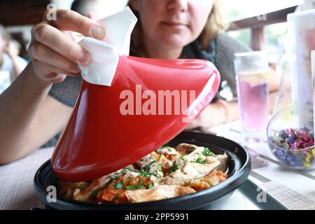 Frau hebt roten Deckel des Tagins im Restaurant Stockfoto