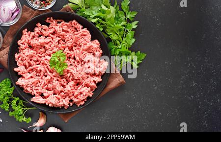 Rohes Rinderhackfleisch auf einem Teller auf schwarzem Steinhintergrund mit Kopierbereich. Draufsicht, flach liegend Stockfoto