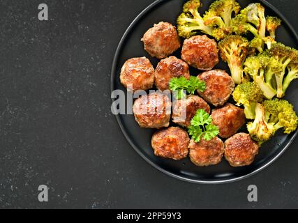 Hausgemachte Schnitzel und gebratener Brokkoli auf Platte auf schwarzem Steinhintergrund mit freiem Textbereich. Draufsicht, flach liegend Stockfoto