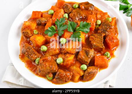 Rindereintopf mit Kartoffeln und Karotten in Tomatensauce auf weißem Teller, Nahaufnahme Stockfoto