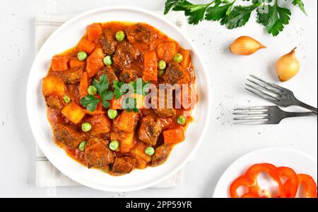 Rindereintopf mit Kartoffeln und Karotten in Tomatensoße auf weißem Steinhintergrund. Draufsicht, flach liegend Stockfoto