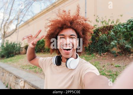 Ein glücklicher afroamerikaner mit Afrohaar, der ein Selfie-Porträt macht. Ein Teenager, der Spaß hat und draußen lacht. Ein fröhlicher Mann mit einem zahnigen Lächeln, der einen Videoanruf hat. Erfolgreicher Universitätsstudent. Hochwertiges Foto Stockfoto