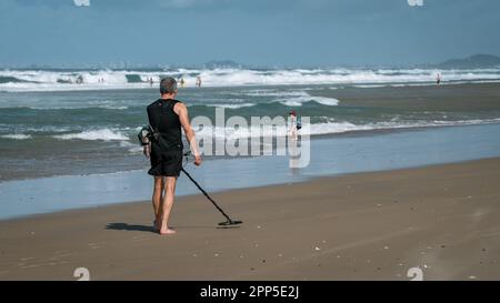 Gold Coast, Australien - Mann, der einen Metalldetektor benutzt, um Wertsachen am Strand zu finden Stockfoto