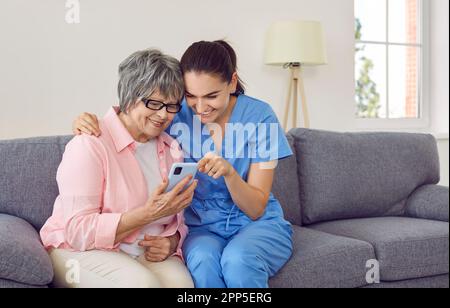 Positive medizinische Sozialarbeiterin, die älteren Frauen beibringt, wie man ein Mobiltelefon benutzt. Stockfoto