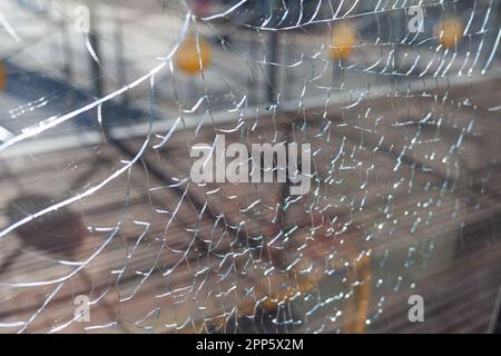 Zerbrochenes Glas, Risse am Fensterglas. Es gibt einen Fluss und eine Stadt im Hintergrund. Vandalismus. Stockfoto