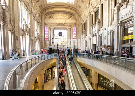 Personen, die eine Rolltreppe im Inneren der Eingangshalle im Erdgeschoss des Mailänder Hauptbahnhofs in Mailand, Italien, fahren Stockfoto