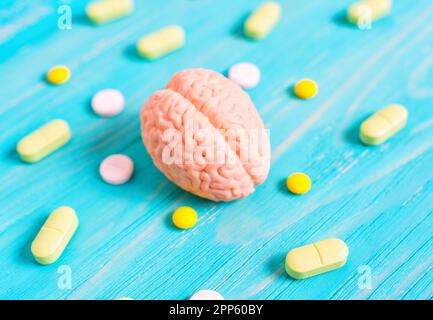 Miniaturmodell des menschlichen Gehirns, umgeben von verstreuten Pillen auf einem blauen Holztisch. Hintergrundinformationen zu medizinischen oder pharmazeutischen Themen in der Präsentation Stockfoto