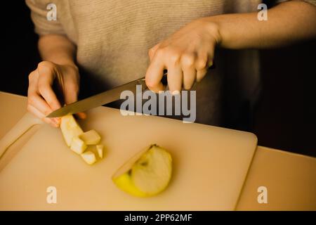 Eine Frau schneidet vorsichtig einen knusprigen Apfel durch und offenbart sein saftiges Fleisch. Dieses Bild hebt Themen wie häusliche Pflege, Ernährung und Einfachheit hervor. H Stockfoto