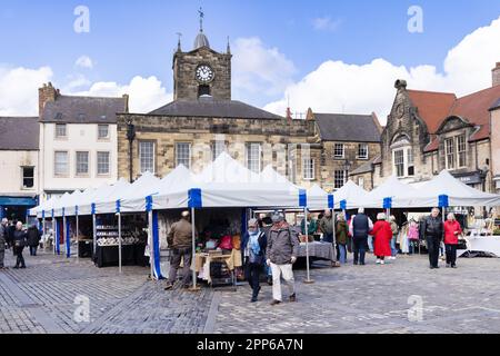 Alnwick Market; Menschen, die an Marktständen auf dem Market Square einkaufen, in der Frühlingssonne; Alnwick Stadtzentrum, Alnwick, Northumberland UK Stockfoto