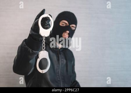 Ein Bandit mit schwarzer Maske und Handschuhen mit Handschellen in den Händen auf weißem Hintergrund. Freilassung aus dem Gefängnis. Gefängnisausbruch-Konzept. Gefängnisausbruch Stockfoto