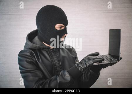 Cyberkriminalität, durchdachtes Hacking und Computerkriminalität - männlicher Hacker im weißen Raum mit Laptop-Computer, Hacker in einer schwarzen Maske mit einem modernen Ultrabook, Stockfoto