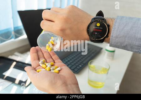 Kranker, reifer Mann, der bei der Arbeit Pillen nimmt. Stress- und Überarbeitskonzept. Ein kranker Geschäftsmann trinkt Beruhigungspillen. Die Smartwatch zeigt das emotionale Stockfoto