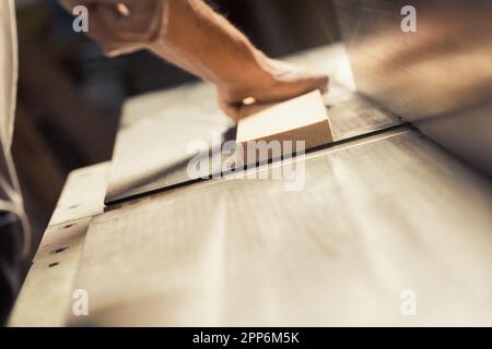 Die starke und muskulöse Hand und der Unterarm eines Zimmermanns, der ein Metallwerkzeug hält und es verwendet, um beim Bau eines Möbelstücks zu helfen, das es sein wird Stockfoto