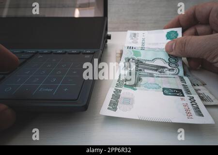 Ein Mann drückt mit dem Finger auf eine Rechnertaste. Mann, der Rubel zählt. Kassenbuchhaltung. Ein Geschäftsmann zählt mit einem Computer Profite. Buchhaltungsberechnung Stockfoto