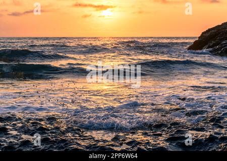 Sonnenuntergang am Strand mit glitzernden Wellen, die gegen das Ufer von Korsika schlagen Stockfoto