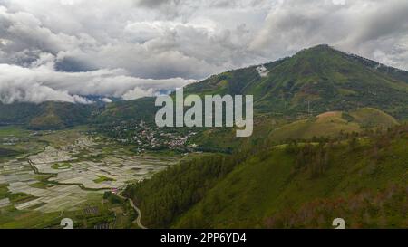 Luftdrohne von Ackerland und Stadt im Tal inmitten der Berge. Sumatra, Indonesien. Stockfoto