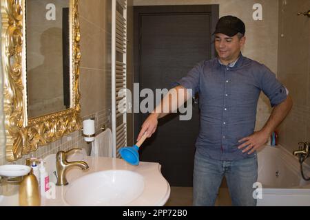 Bild eines Klempners in einem Badezimmer, der mit einem Stößel auf ein verstopftes Waschbecken zeigt, das repariert werden muss. Heimwerkerarbeit zu Hause. Stockfoto