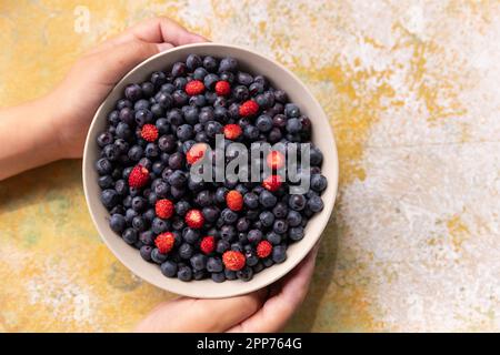 Erdbeeren und Blaubeeren in einer Schüssel auf einem rustikalen Holztisch. Diese Super-Food Beeren sind Teil einer gesunden Ernährung, die ein gesundes Herz und gut fördert Stockfoto