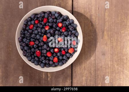 Erdbeeren und Blaubeeren in einer Schüssel auf einem rustikalen Holztisch. Diese Super-Food Beeren sind Teil einer gesunden Ernährung, die ein gesundes Herz und gut fördert Stockfoto