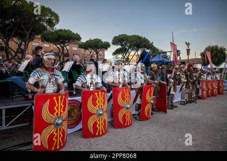 Soldaten aus dem antiken Rom stellten sich während des Konzerts der italienischen Armeeband in Schlange. Figuren aus der ganzen Welt, die durch ihre Leidenschaft für die Welt des antiken Roms vereint sind, haben ein altes Dorf am Circus Maximus gegründet, um den 2776. Jahrestag der Gründung Roms zu feiern. An der von der Gruppo Storico Romano, einer gemeinnützigen Kulturvereinigung, die 1994 aus Leidenschaft für das antike Rom geboren wurde, organisierten Veranstaltung nahmen in diesem Jahr 2500 Nachspieler Teil, die 80 Verbänden aus 16 Nationen angehören. Die meisten Reendarsteller kommen aus Spanien. Der Tag endet mit einem Konzert von The IT Stockfoto