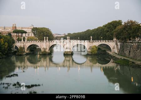 Sonnenuntergang über dem Tiber in Rom, Italien, an einem bewölkten Abend mit Reflexion im Wasser, während Sie bei einem europäischen Urlaub über die Brücke gehen Stockfoto