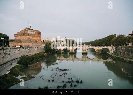 Sonnenuntergang über dem Tiber in Rom, Italien, an einem bewölkten Abend mit Reflexion im Wasser, während Sie bei einem europäischen Urlaub über die Brücke gehen Stockfoto