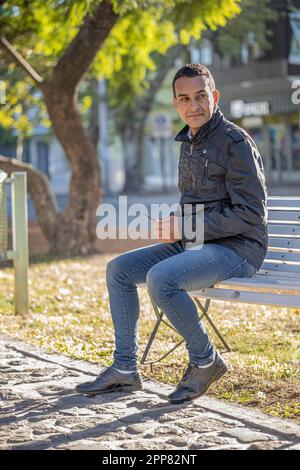 Ein junger latino, der auf einer quadratischen Bank sitzt. Stockfoto