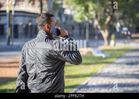 Junger Latino-Mann, der mit dem Handy spricht, von hinten gesehen, mit Kopierraum. Stockfoto