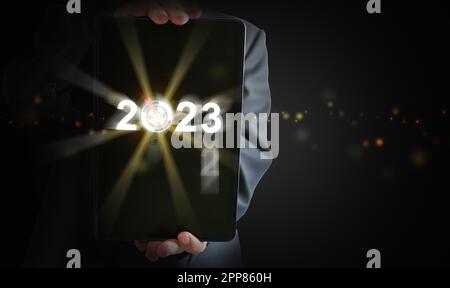 Die Hände eines Geschäftsmanns halten ein Tablet und das Jahr ändert sich von 2022 auf 2023. Zeit für den Start ins neue Jahr, Geschäft, Projekt, Pfad, Ziel, Oder das Leben. Stockfoto