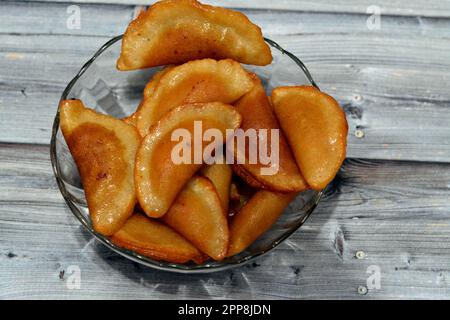 Eine Schüssel mit Qatayef-Knödeln gefüllt und gefüllt mit Nüssen und zerkleinerten Kokosnüssen, in tiefem Öl gebraten und mit Zuckersirup getränkt, arabischer Dessert gefaltet Pfanne Stockfoto