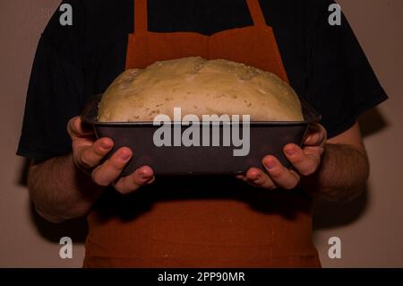 Baker in Schürze mit einem selbstgemachten Brotteig. Eine altmodische Bäckerei. Weltküche - Brot und Backwaren Stockfoto