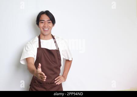 Porträt eines attraktiven asiatischen Barista in brauner Schürze, der nach einem Händedruck streckt und jemanden begrüßt. Isoliertes Bild auf weißem Hintergrund Stockfoto