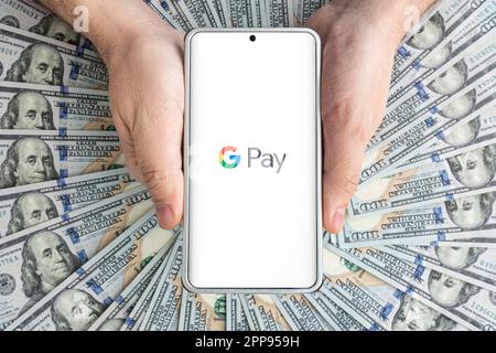 Dollars und Smartphone mit Google Pay-Logo auf dem Bildschirm. Google Pay ist ein mobiler Zahlungs- und digitaler Brieftaschendienst von Google. 30. März 2023. Barnau Stockfoto