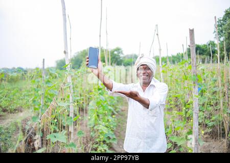 Ein indischer glücklicher Bauer, der sein Handy in der Hand hält Stockfoto