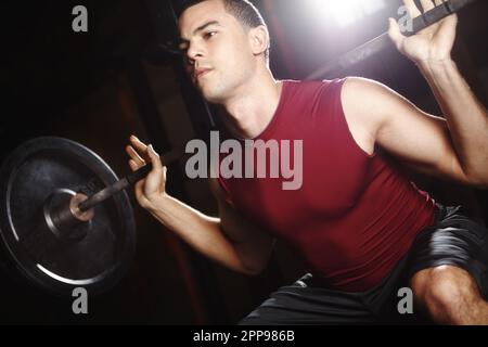Kein Problem, die schweren Gewichte zu heben. Ein gutaussehender junger Mann, der eine Hantel aus der Hockposition hebt. Stockfoto