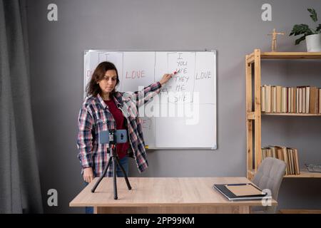 Eine Lehrerin unterrichtet online Englisch für Kinder über ein Mobiltelefon im Klassenzimmer zu Hause und filmt einen Lehrvortrag. Online-Streaming Stockfoto