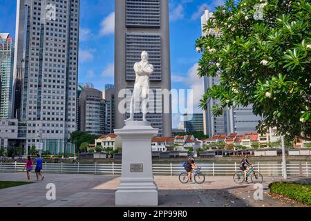Eine Statue von Sir Stamford Raffles am Raffles Landing Pier, Boat Quay, Singapore River, Singapur; b/g: Die Skyline des Geschäftsviertels von Singapur Stockfoto
