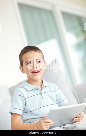 Ich liebe dieses Spiel. Vertikales Bild eines kleinen Jungen, der sich auf einem digitalen Tablet unterhält. Stockfoto