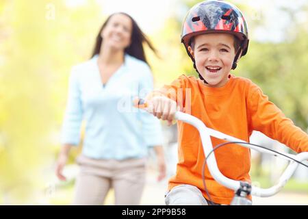 Du hast es geschafft. Eine alleinerziehende Mutter, die ihren Sohn zum ersten Mal Fahrrad fahren sieht. Stockfoto