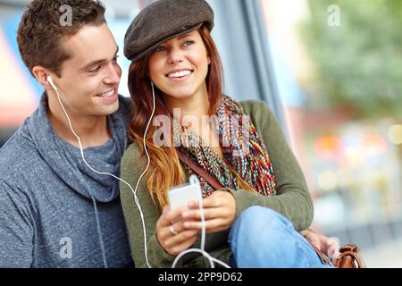 Gemeinsame Nutzung eines Kopfhörers. Ein glückliches Paar, das Musik auf einem Telefon hört, zusammen mit Copyspace. Stockfoto