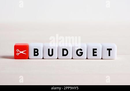 Budgetkürzungskonzept. Kostensenkung und Finanzstabilität. Kürzung des Familienbudgets. Ausgaben senken. Scheren-Symbol und das Wort Budget auf Würfeln. Stockfoto