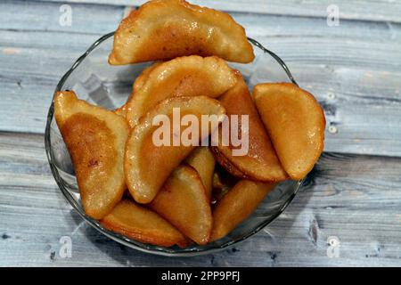 Eine Schüssel mit Qatayef-Knödeln gefüllt und gefüllt mit Nüssen und zerkleinerten Kokosnüssen, in tiefem Öl gebraten und mit Zuckersirup getränkt, arabischer Dessert gefaltet Pfanne Stockfoto