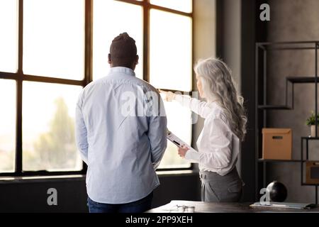 Frau, Die Mit Männlichem Zeigefinger Am Fenster Im Büro Spricht Stockfoto