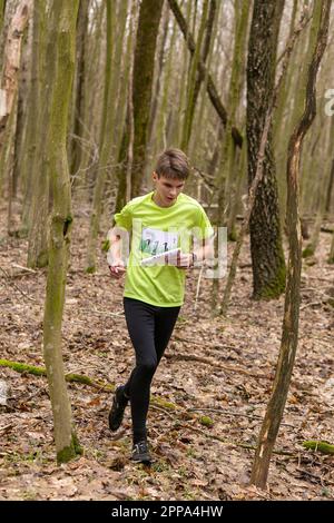 Grivki, Weißrussland - 26. März 2023: Starker kaukasischer Teenager in Sportbekleidung, der während des Trainings im Outdoor-Orientering Gro durch einen Wald läuft Stockfoto