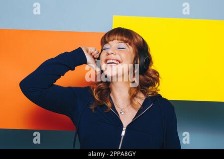 Frau, die Musik über kabellose Kopfhörer in einem Designstudio hört. Glückliche junge Frau mit bunten geometrischen Formen. Stockfoto