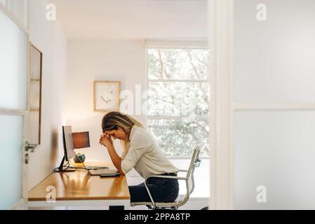 Junge Geschäftsfrau, die Kopfschmerzen in ihrem Büro hat. Überlastete Geschäftsfrau, die vor einem Notebook sitzt und bei der Arbeit müde wird. Stockfoto