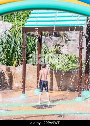 Asiatischer kleiner Junge, der im Sommer mit dem Wasser im Brunnen des Parks spielt Stockfoto