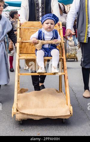 Huelva, Spanien - 18. März 2023: Ein Baby fährt in einer rustikalen, mit historischen Kostümen verkleideten Kinderwagen in der Parade der mittelalterlichen Discove Stockfoto