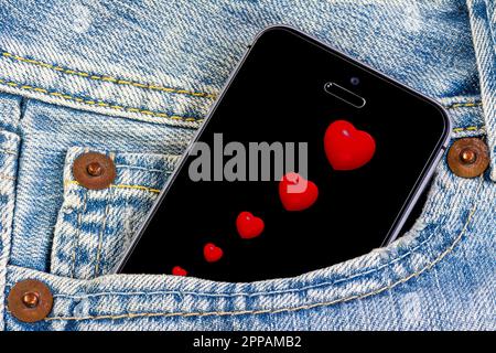 Smartphone mit roten Herzen auf dem Bildschirm in einer Jeans-Tasche Stockfoto